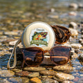 Sunglasses with a 'Fish Juice' product on a rock by a water body