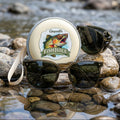 Sunglasses with a 'FishJuice' container on rocks by a stream